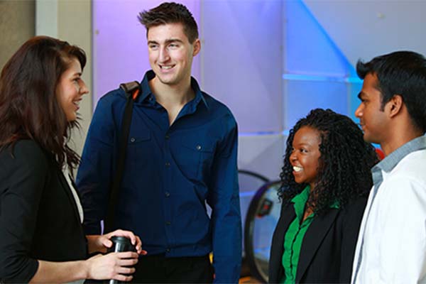 Four students standing beside the Aldred Centre escalating having a conversation.