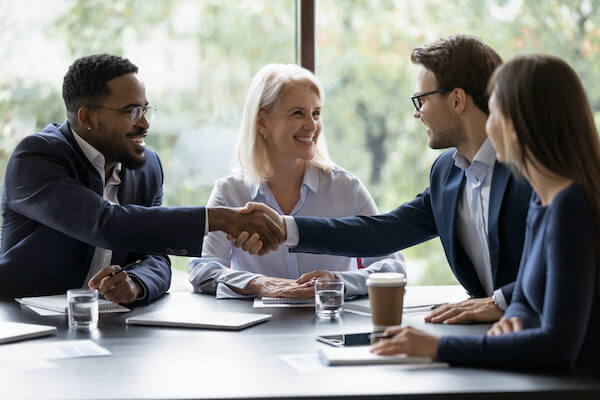 A group of people wearing business formal attire shake hands while sitting around a table.