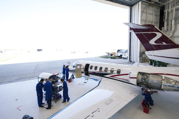 A group of people gather outside an airplane inside the Art Smith Aero Centre hangar.