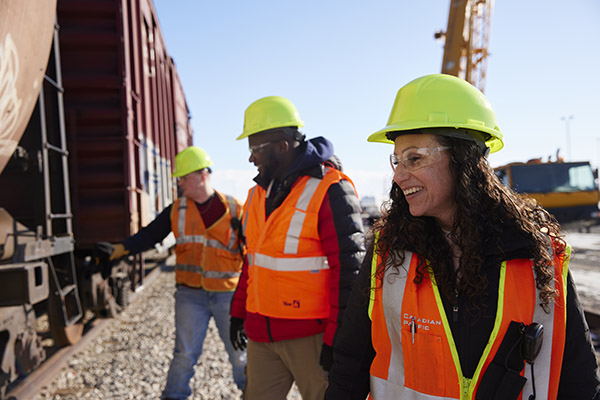 Three students wearing hardhats and safety vests stand beside a rail car at SAIT's Centre for Rail Training and Technology.
