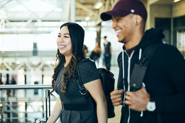 Two students wearing back packs walk past the camera