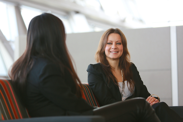 Two women sitting in soft chairs in an office having a conversation.
