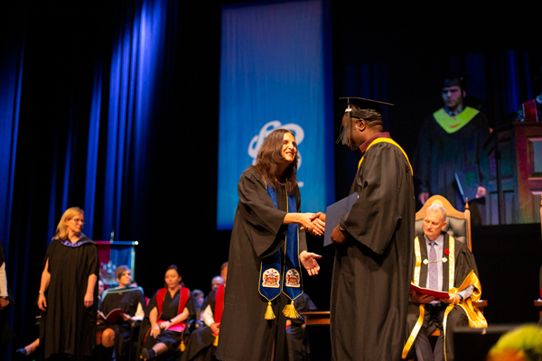 student in a graduation gown crossing the stage