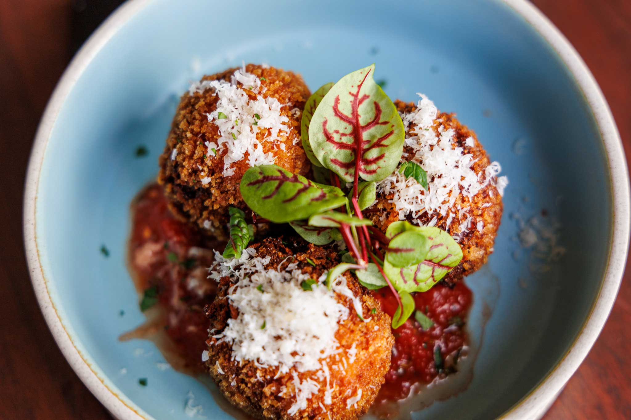 three fried arancini balls with marinara sauce, grated parmesan, and micro greens