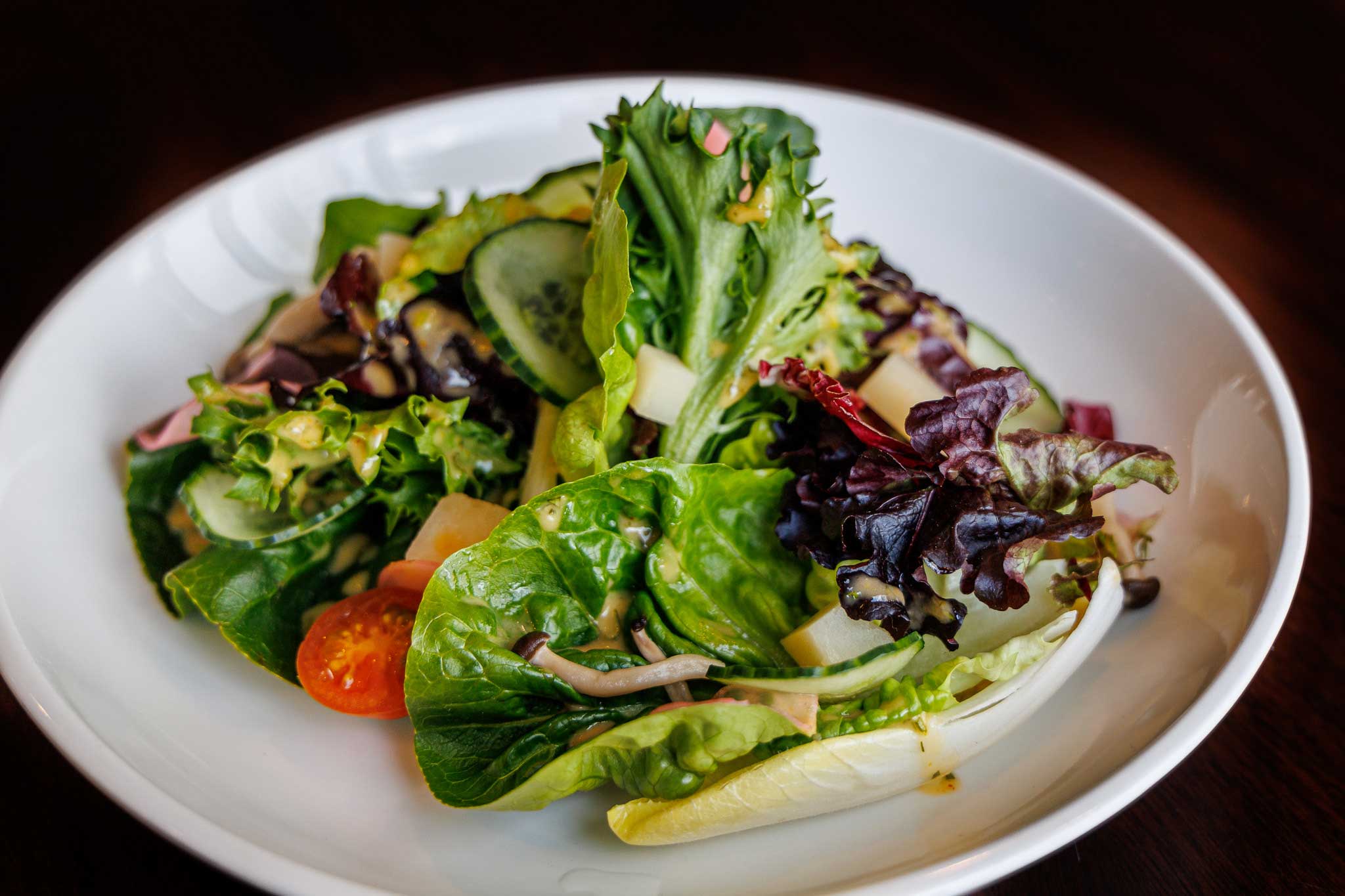 assorted green lettuce, tomato and cucumber on a white plate