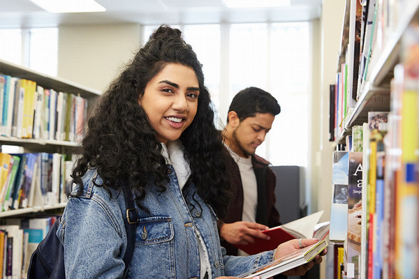 Students looking at books from a library shelf.