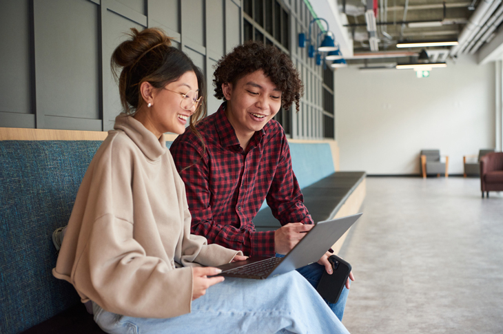 Two students discussing while looking at a laptop