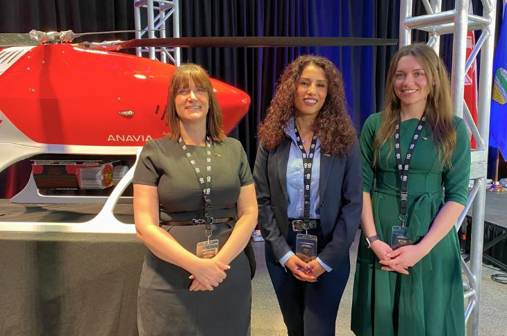 Three females standing and smiling in front of a drone helicopter