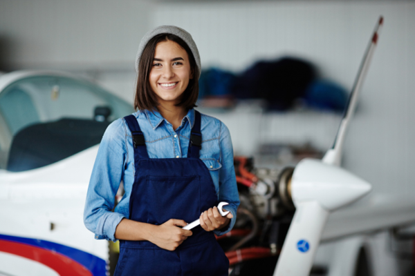 A woman smiling holding a wrench with an airplane in the background