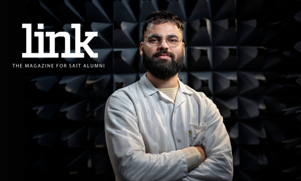 grad standing in front of dark background with arms crossed.