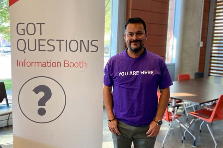 Volunteer at New Student Orientation standing by a sign